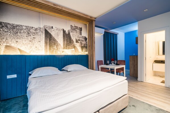 Een hotelkamer met een groot bed, een bureau met stoel, een kleine tafel met stoel, en een badkamer zichtbaar door een geopende deur.