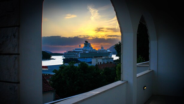 A view of a cruise ship at sunset through an arched window overlooking a body of water and a mountainous landscape. - Apartments Tayra - Comfort Studio with Balcony (BR3) (Dubrovnik)