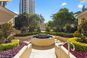 A courtyard with a central fountain, surrounded by well-maintained hedges and palm trees.