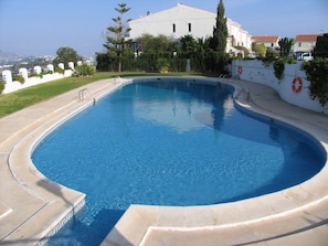 Una piscina con borde curvo, rodeada por un muro bajo con flotadores salvavidas, con edificios y follaje como fondo.