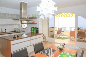 Cocina moderna con una isla central, comedor con mesa y sillas, y balcón con mobiliario exterior.