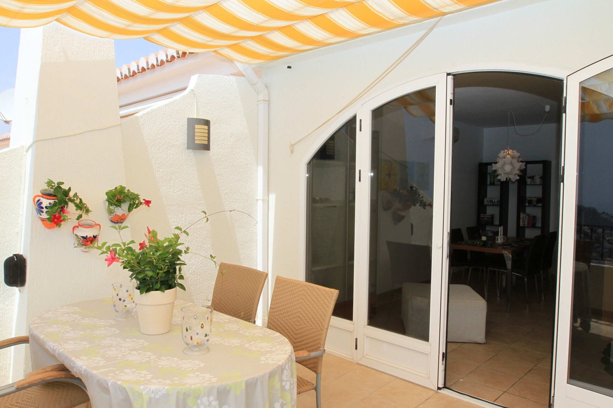 A patio with a table, chairs, potted plants, and a sliding glass door leading to an indoor area.