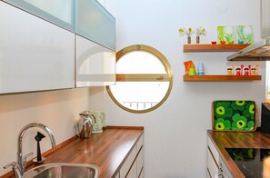 Una cocina con un ventanal redondo, electrodomésticos de acero inoxidable, encimeras de madera y un estante con objetos decorativos.