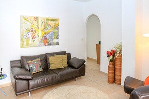Una sala de estar con un sofá de cuero marrón, un cuadro abstracto de colores y dos altos jarrones de mimbre con flores.