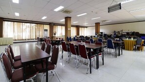 Une grande salle de conférence dotée de nombreuses tables et chaises, équipée de luminaires au plafond et de la climatisation.
