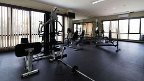 Une salle de sport équipée de divers appareils d’exercice, dotée de grandes fenêtres et d’un sol plat.