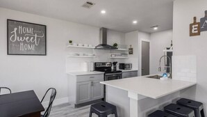 Una cuina moderna amb una illa central, armaris blancs i una zona de menjador amb taula i cadires.