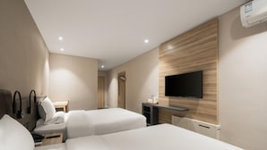 Habitación de hotel con dos camas, un escritorio, un televisor de pantalla plana montado en la pared y una pared decorativa de madera.