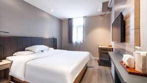 Habitación de hotel con cama, escritorio, silla, televisor de pantalla plana y ventana con cortinas.