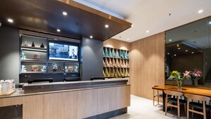 Un moderno mostrador de recepción con pantalla digital, una zona de estar con mesa y sillas de madera, y una pared con exhibición de objetos doblados.