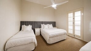 Quarto com duas camas, um ventilador de teto, mesa de cabeceira e janela com vidro fosco.