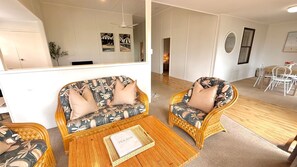 Um quarto com dois sofás de vime, uma mesa de centro de madeira e uma área de jantar com uma mesa e cadeiras brancas.
