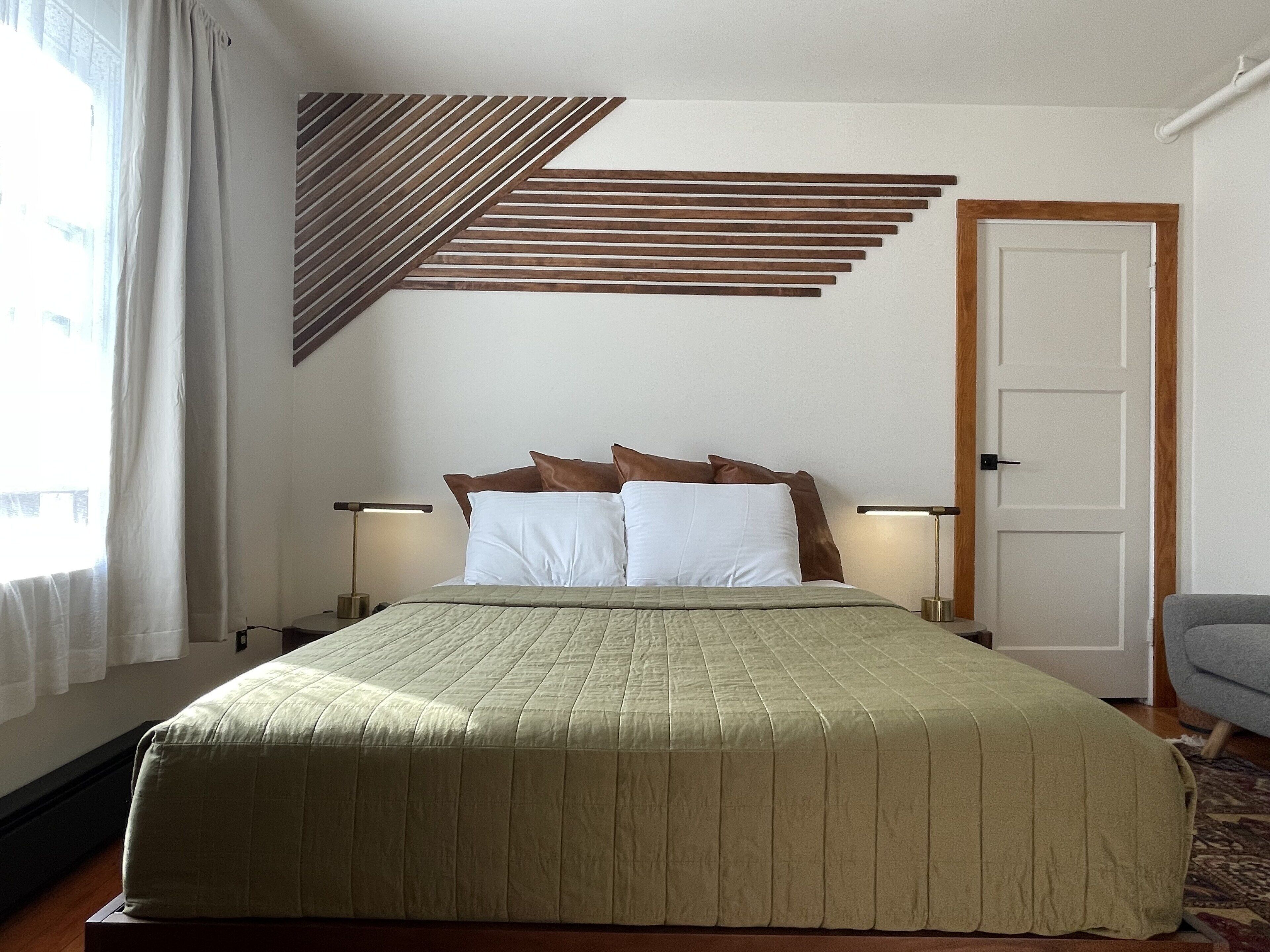 Cama bem arrumada com colcha verde, duas luminárias de cabeceira e decoração de parede em ripas de madeira.