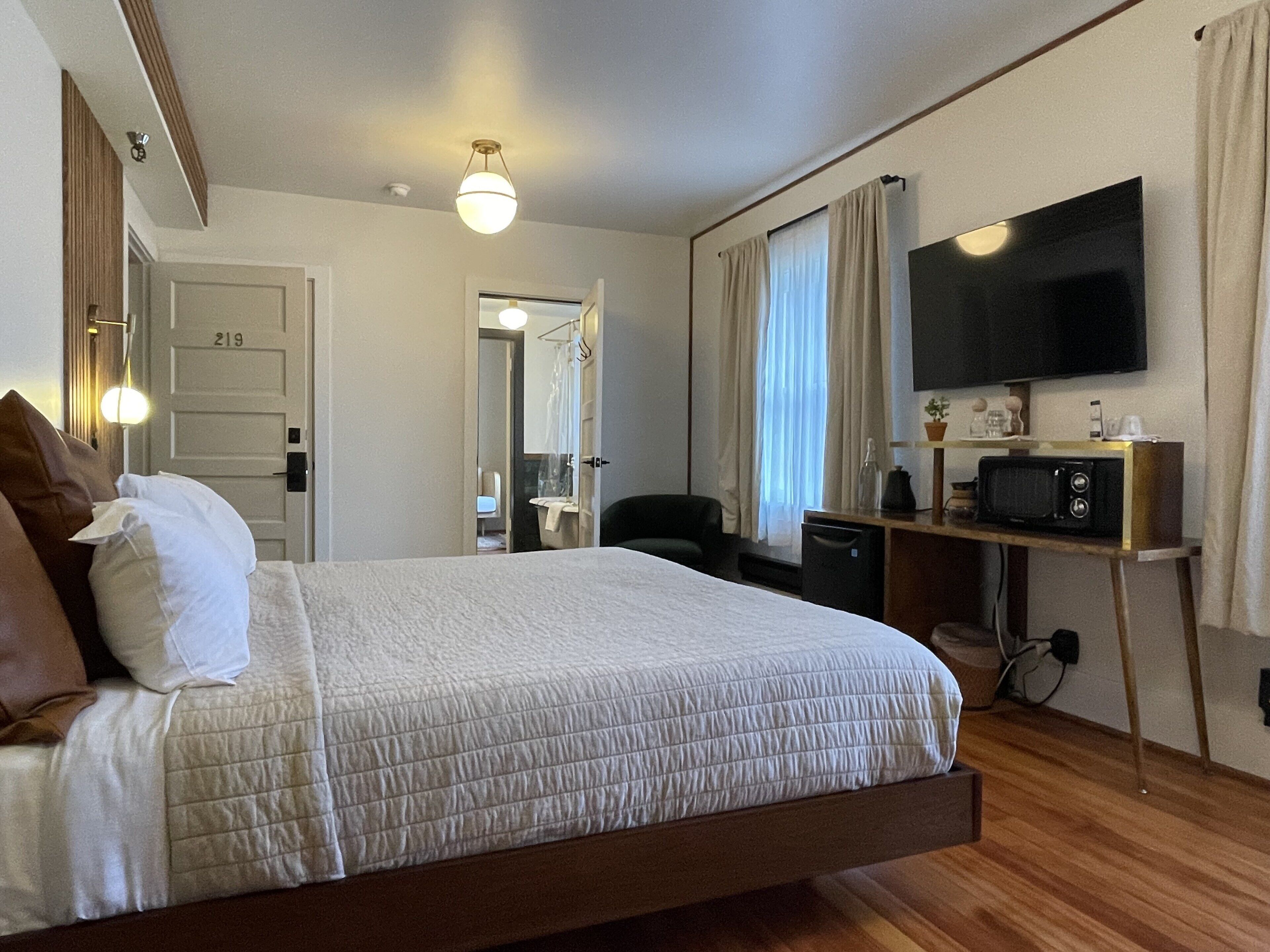 Une chambre d’hôtel avec un lit, un bureau doté d’une télévision, un four à micro-ondes et une salle de bain visible à travers une porte ouverte.