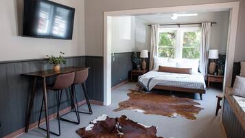 A bedroom with a bed, a desk with two chairs, a television, and a cowhide rug.