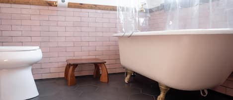 A bathroom with a white toilet, a wooden stool, and a freestanding bathtub.