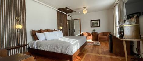 A modern bedroom with a large bed, wooden floor, and a desk area with a mirror and small table.
