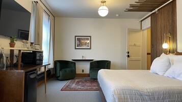 A hotel room with a bed, desk, two chairs, a TV, and a small kitchenette.