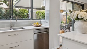 Eine moderne Küche mit weißen Schränken, einem Edelstahl-Geschirrspüler und einem Fenster mit Blick auf einen Garten.