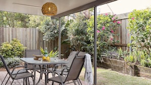 Eine Terrasse im Freien mit Tisch und Stühlen, umgeben von einem Holzzaun und verschiedenen Pflanzen.