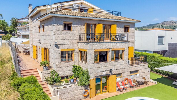 A multi-story stone building with a pool, outdoor seating, and a view of the surrounding landscape.
