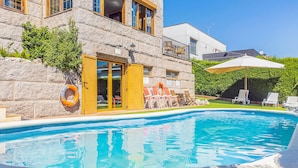 A swimming pool with a stone building in the background, a covered patio area, and outdoor seating.