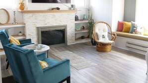 Una sala de estar con chimenea, televisor de pantalla plana y sillones azules.