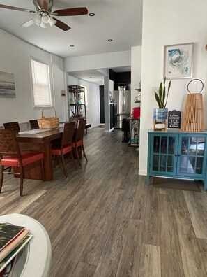 A spacious dining area with wooden chairs and a table, a kitchen with modern appliances, and a blue cabinet with decorative items.