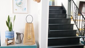 Una escalera con peldaños negros y barandilla de metal, un mueble de color turquesa con puertas de cristal, un cuadro abstracto enmarcado y una cesta de mimbre en la pared.