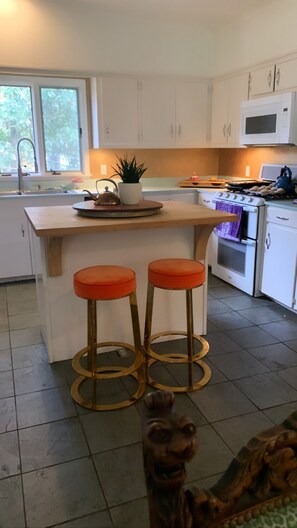 A modern kitchen with white cabinets, a wooden island with two stools, a microwave, and a stove.