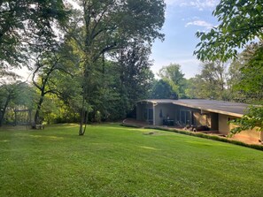 A house with a covered patio, surrounded by a well-maintained lawn and trees.