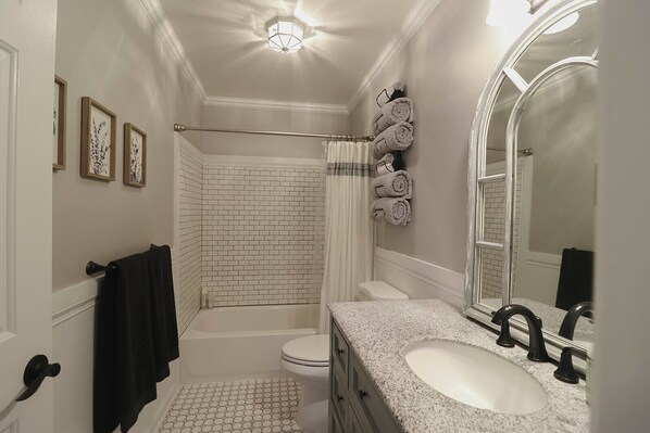 A bathroom with a white subway tile shower, a white toilet, a granite countertop sink, and a large mirror.