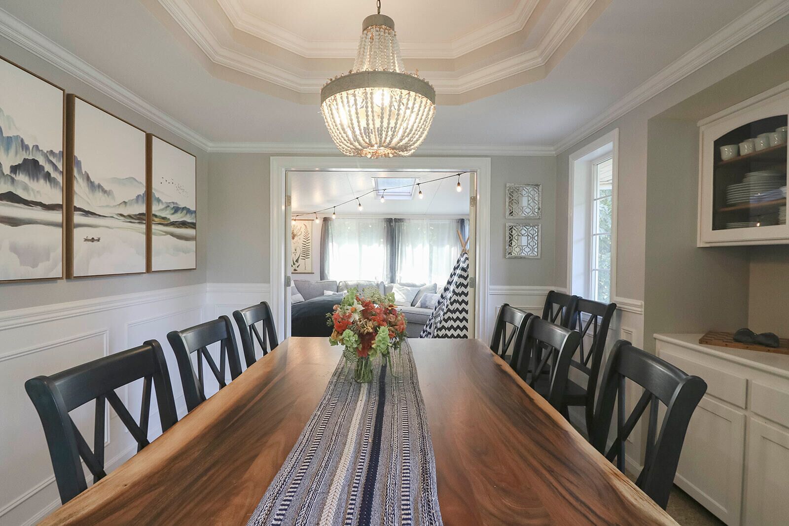 Ein Esszimmer mit einem Holztisch, schwarzen Stühlen, einer Chandelier und Kunstwerken an den Wänden.