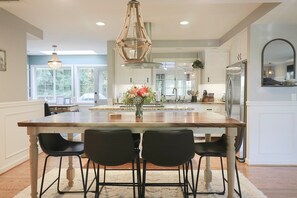 A modern kitchen with a large island, black bar stools, a chandelier, and a refrigerator. - Classy, Spacious Home, Family Friendly, 3 bed 2 bath W/ Hot Tub!  (Port Angeles)
