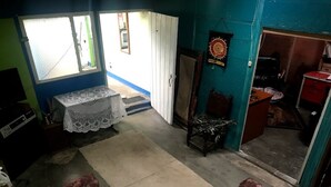 Une pièce comprenant un lit, une table recouverte d’une nappe en dentelle, une chaise et une porte donnant sur une autre pièce.