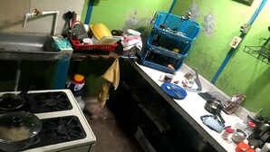 Une cuisine équipée d’une cuisinière à gaz, d’un évier et de divers ustensiles de cuisine. On y trouve des caisses bleues et un saladier jaune sur le plan de travail.