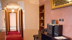 Un corridoio con tappeto rosso, porte in legno, soffitto decorato e impianto audio a parete.