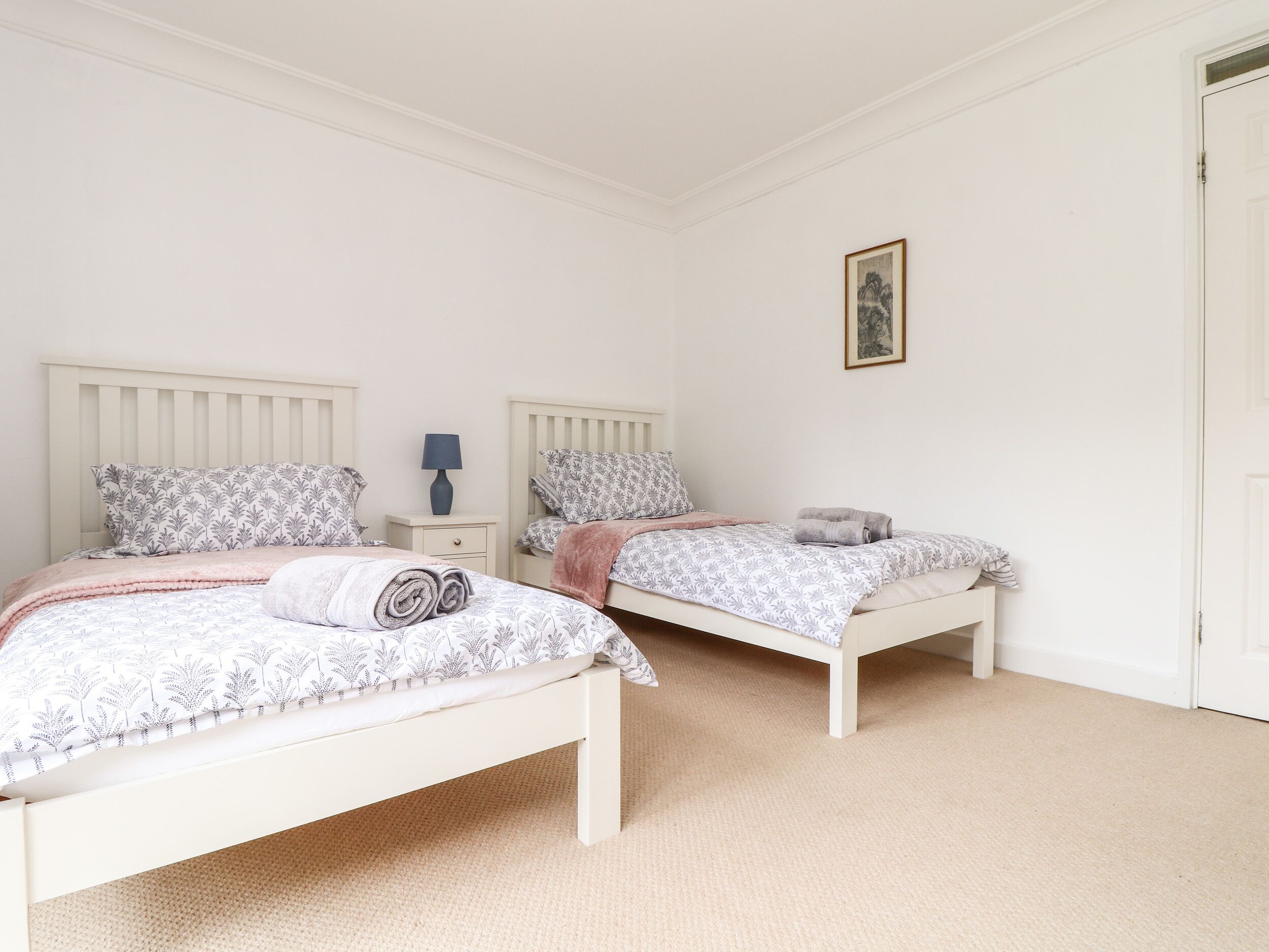 A bedroom with two beds, each with patterned bedding and pillows, a nightstand with a lamp, and a framed picture on the wall.
