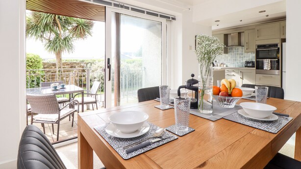 A dining area with a wooden table, chairs, and a view of the garden through glass doors. - The Wesley Apartment (Falmouth)