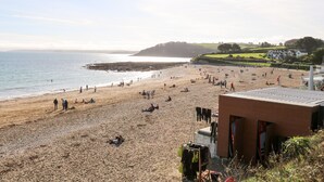 A beach with people sunbathing and walking. There is a building with a red roof and a clothesline with clothes hanging. - The Wesley Apartment (Falmouth)
