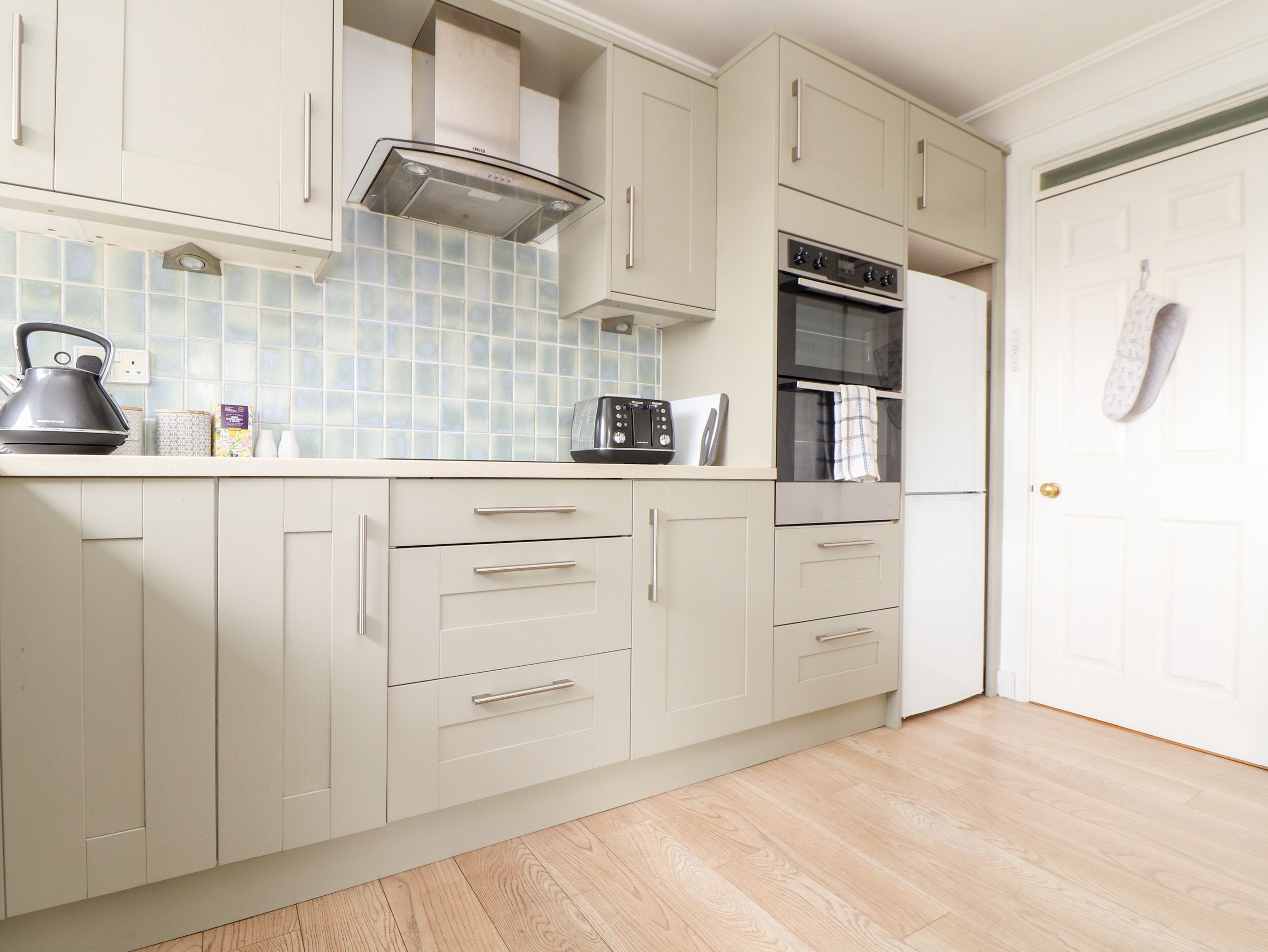 A kitchen with light-colored cabinets, a microwave, toaster, kettle, and a tiled backsplash.