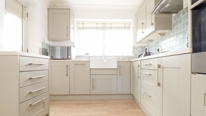 A kitchen with light-colored cabinets, a microwave, and a sink. - The Wesley Apartment (Falmouth)