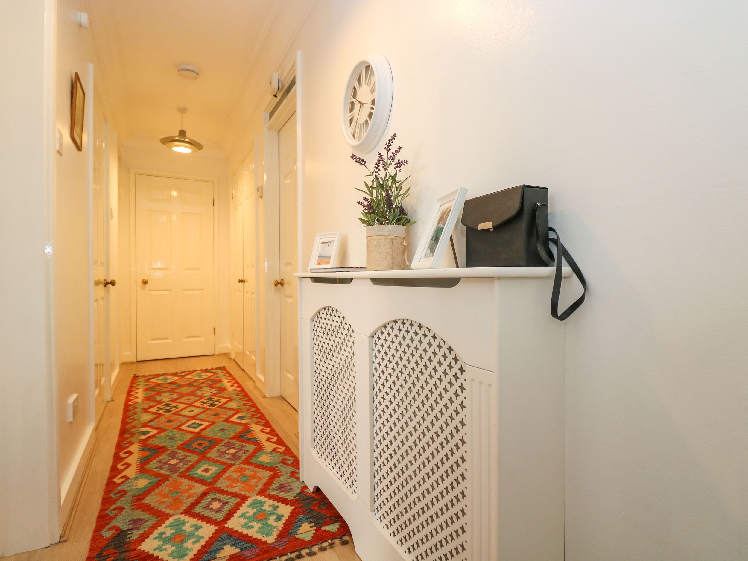 A hallway with a patterned rug, a white cabinet with decorative elements, and a clock on the wall.