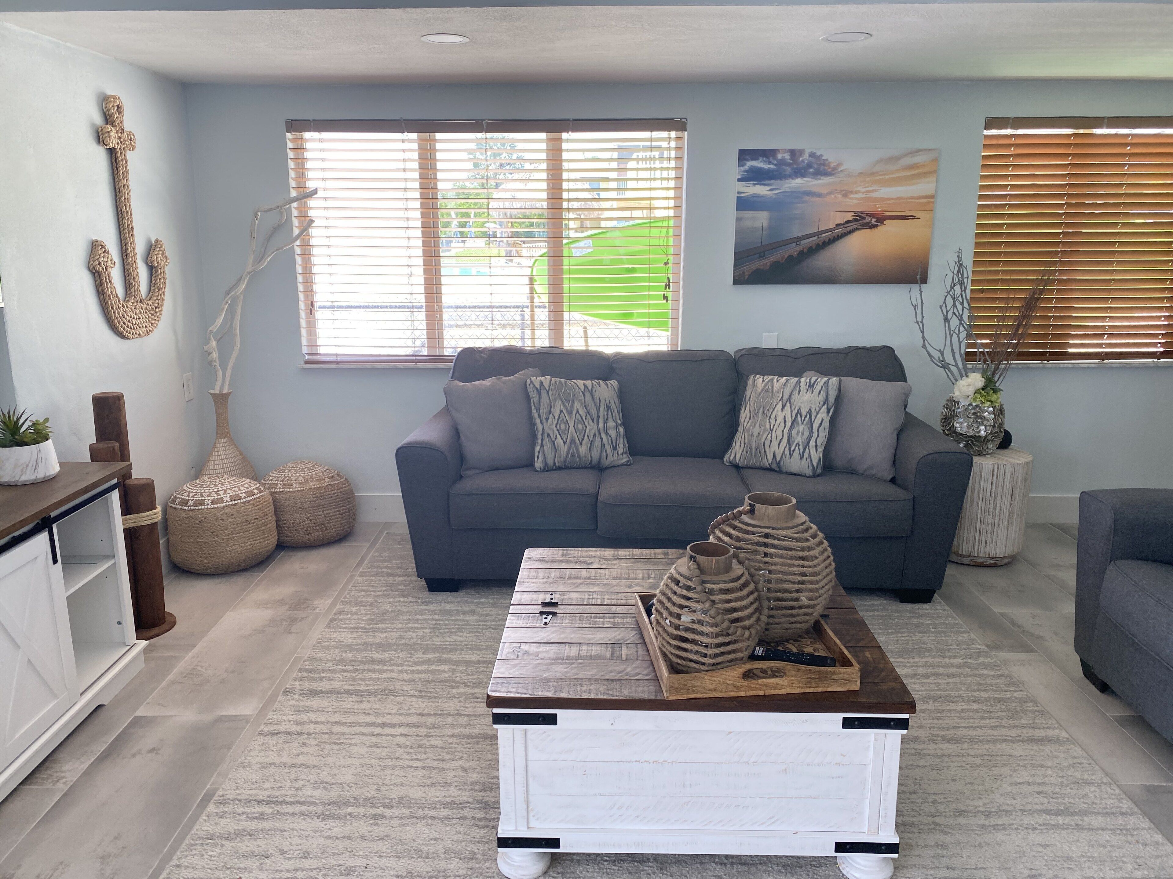 A living room with a grey sofa, a wooden coffee table, and a large window with blinds.