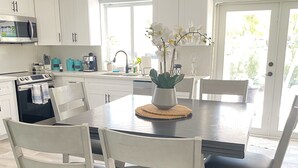 Une cuisine moderne avec des meubles blancs, un coin repas avec des chaises blanches et une vue sur l’extérieur.