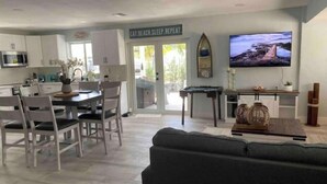 Un salon moderne comprenant un canapé, un coin repas avec des chaises et une table, une cuisine avec des placards et un four à micro-ondes, et un téléviseur fixé au mur.