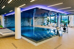 An indoor swimming pool with a modern design, surrounded by lounge areas and potted plants. - Elexus Poiana Brasov (Brasov)