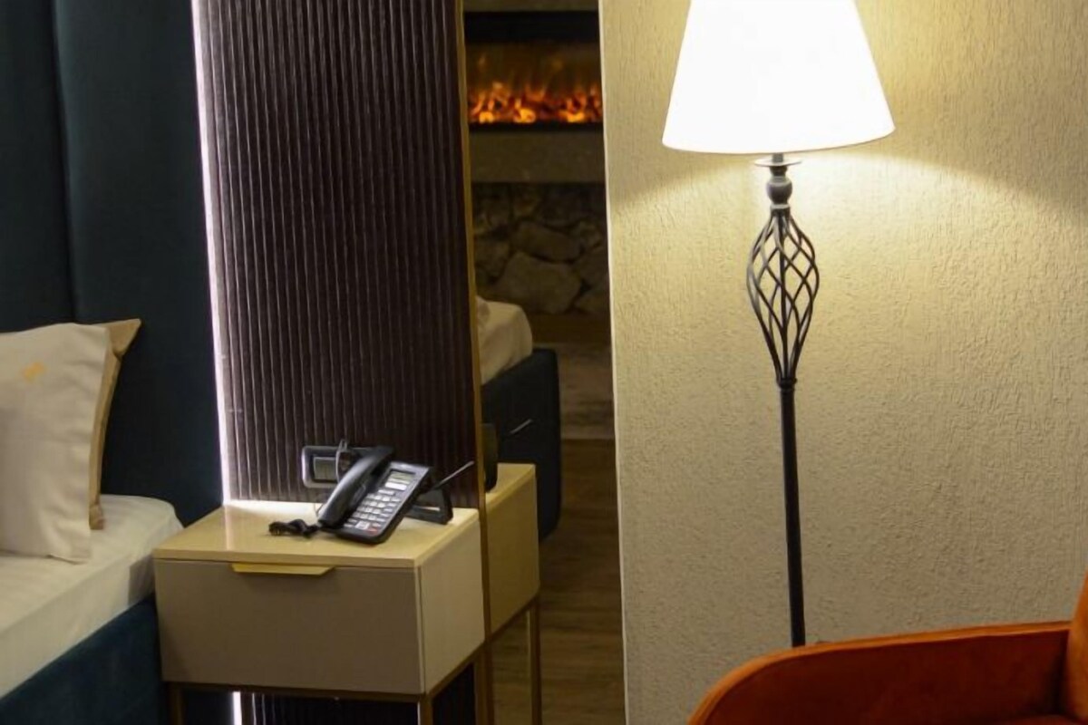 A hotel room with a bed, a bedside table with a telephone, a lamp, and a chair.
