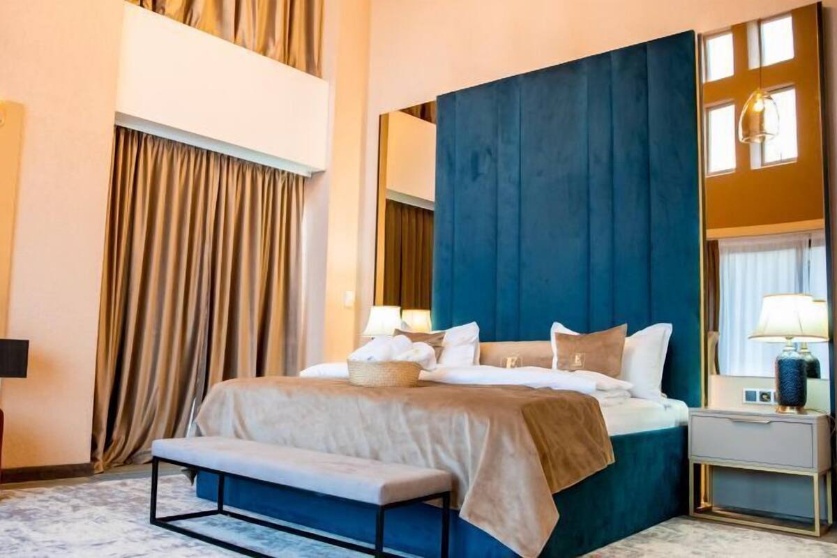 A modern hotel room with a large bed, a bench, a desk, and a chair.