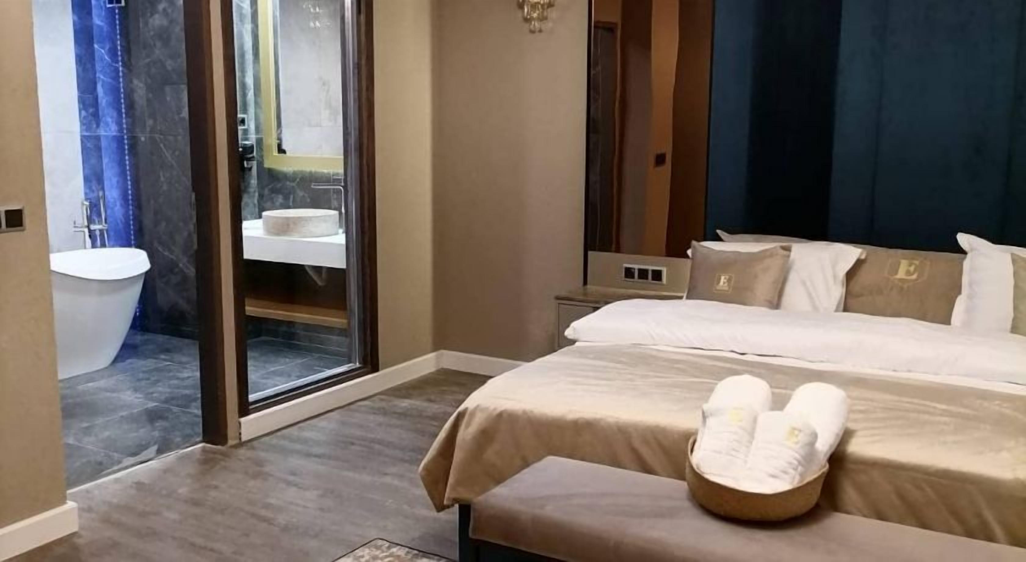 Une chambre d’hôtel avec un grand lit, une salle de bain avec baignoire et une porte-fenêtre coulissante donnant sur un balcon.